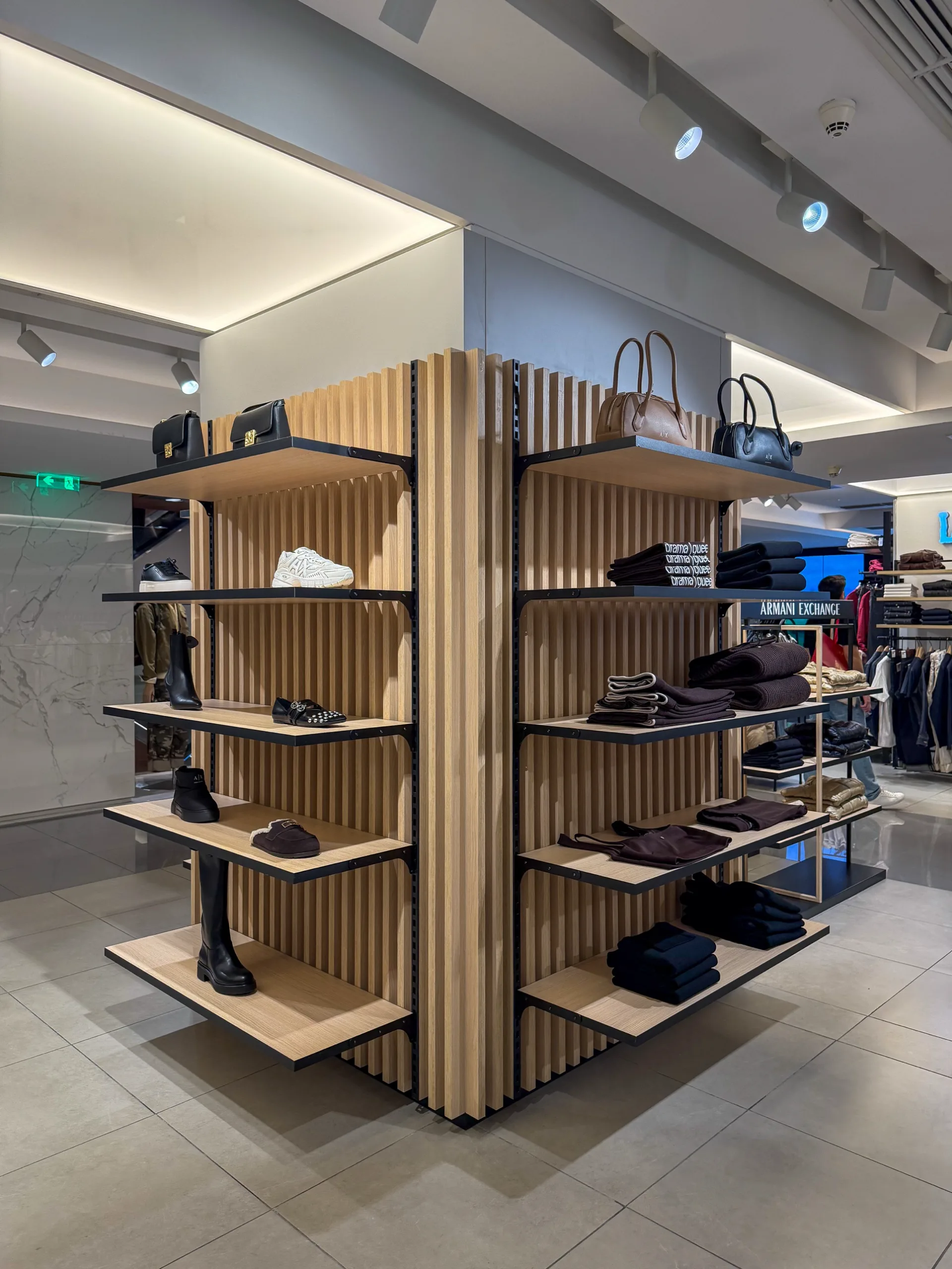 Armani Exchange shop-in-shop at attica City Link with oak-effect slat walls, black metal shelving and mirror-clad tables by Spanopoulos Furniture.